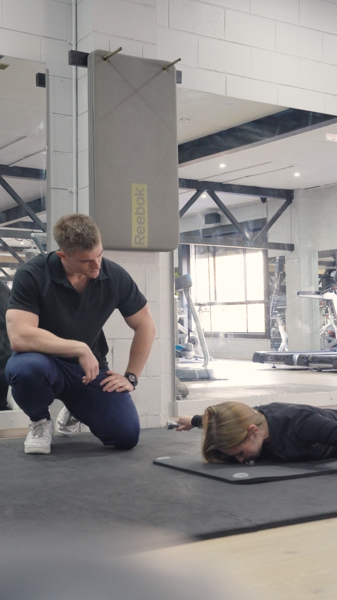 Remy coaching a client through a floor exercise in the gym